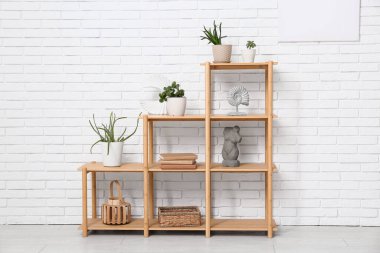 Süslü raflar, dekorasyon ve kitaplarla dolu beyaz tuğla duvarın yanındaki oda.