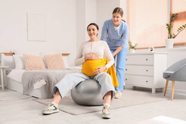 Eşarplı genç Doula, yatak odasında spor salonunda hamile kadına masaj yapıyor.