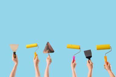 Mavi arka planda boya silindirli ve macun bıçaklı bir sürü el.