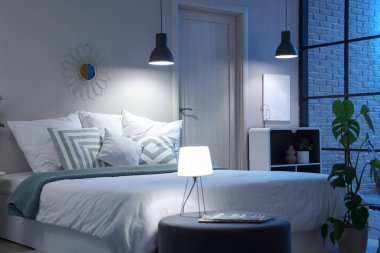 Geceleri rahat yatağı, çiçekleri ve parlayan lambaları olan modern yatak odasının içinde.