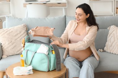Hamile bir kadın doğum çantasına bebek kıyafetleri koyuyor.