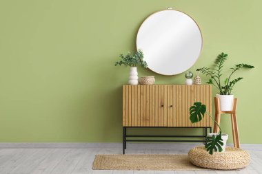 Dekorlu çekmeceler, ev bitkileri ve odadaki yeşil duvardaki ayna.