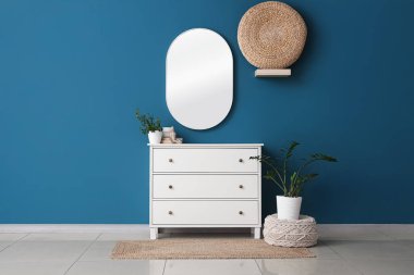 Dekorlu çekmeceler, ev bitkileri ve mavi duvardaki ayna.