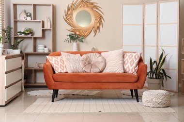 Modern oturma odasının içinde kahverengi kanepe, raf ünitesi ve şık bir ayna var.