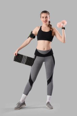 Hafif arka planda dambıl ve köpük silindirli genç bir kadın.