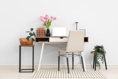 Tabureler, ev bitkileri, dizüstü bilgisayarlar ve vazoda güzel lale çiçekleri olan modern işyerinin içini.