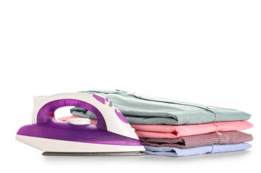 Beyaz arka planda katlanmış temiz gömlek yığınıyla modern elektrikli ütü