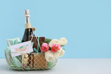 Anneler Günü için şampanya şişesi, lale ve kozmetik sepetleri mavi arka planda beyaz masada.