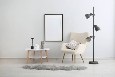 Rahat koltuk, yer lambası ve odadaki gri duvarda asılı boş fotoğraf çerçevesi.