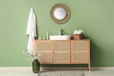 Banyonun içindeki yeşil duvarın yanında çiçek açan dallarla dolu çekmeceler ve vazolar.