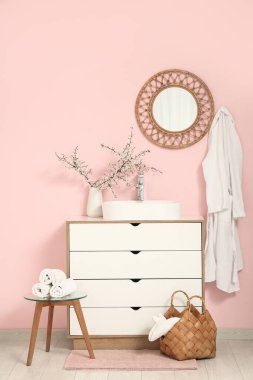 Banyonun içinde, pembe duvarın yanındaki çekmecelerin üstündeki vazoda çiçek açan dallar var.