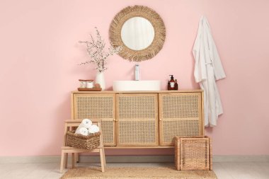 Banyonun içinde, pembe duvarın yanındaki çekmecelerin üstündeki vazoda çiçek açan dallar var.