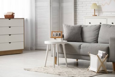 Oturma odasının içinde kanepe, dergi standı ve masada takvim var.