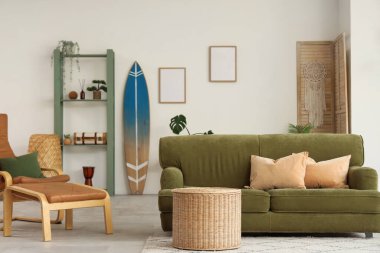 Oturma odasının içinde sörf tahtası, yeşil kanepe ve raf ünitesi var.