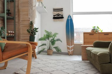 Oturma odasının içinde sörf tahtası, katlanan ekran ve bitkiler var.