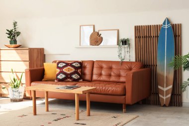 Oturma odasının içinde sörf tahtası, katlanır perde ve kahverengi kanepe var.