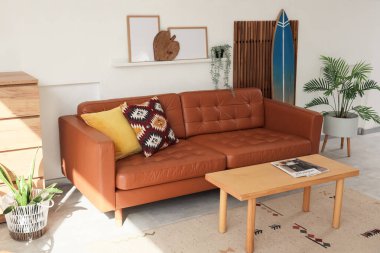 Oturma odasının içinde sörf tahtası, katlanır perde ve kahverengi kanepe var.