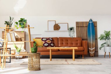 Oturma odasının içinde sörf tahtası, katlanır perde ve kahverengi kanepe var.