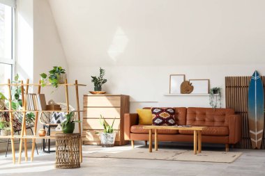 Oturma odasının içinde sörf tahtası, katlanır perde ve kahverengi kanepe var.