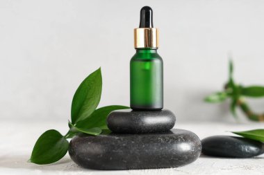 Temel yağ şişesi, spa taşları ve bitki yapraklarıyla aydınlatma masasında kompozisyon