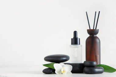 Temel yağ şişesi, sazlık dağıtıcı ve hafif arka planda spa taşlarıyla bileşim
