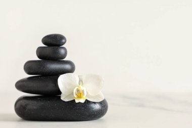 Siyah spa taşları ve açık arkaplanda güzel bir orkide çiçeği yığını.