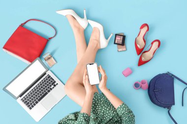 Laptop ve cep telefonu kullanan mavi arka planda güzellik aksesuarları olan bir kadın.