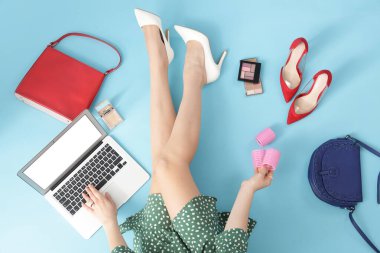 Mavi arka planda güzellik aksesuarları olan dizüstü bilgisayar kullanan bir kadın.