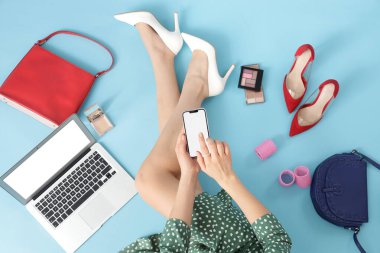 Laptop ve cep telefonu kullanan mavi arka planda güzellik aksesuarları olan bir kadın.