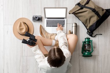 Hafif ahşap zeminde aksesuarlı dizüstü bilgisayar kullanan kadın gezgin.