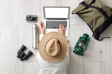 Hafif ahşap zeminde aksesuarlı dizüstü bilgisayar kullanan kadın gezgin.