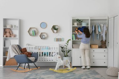 Bebek odasındaki raftan oyuncak alan genç bir kadın.