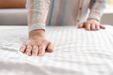 Genç bir kadın hafif yatak odasında yatak yapıyor, yakın plan.