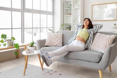 Evdeki kanepede dinlenen gülümseyen genç kadın.