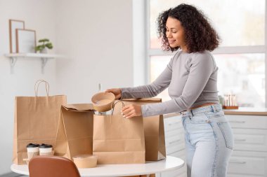 Genç Afro-Amerikalı kadın mutfaktaki kese kağıdından konteynır alıyor. Yemek dağıtım servisi.