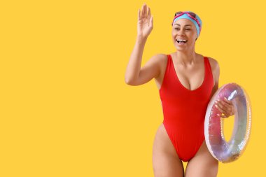 Sarı arka planda şişirilebilir halka sallayan Afro-Amerikan yüzücü kadın.