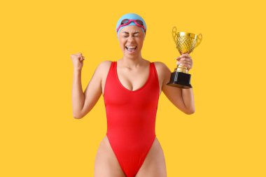 Sarı arka planda altın kupası olan mutlu Afro-Amerikan yüzücü.