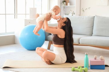 Küçük bebeğiyle evde yoga minderinde oturan sportif genç bir kadın.