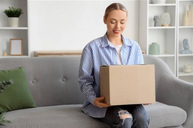 Paket kutulu genç bir kadın evdeki kanepede oturuyor.