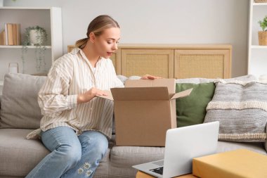 Genç bir kadın evdeki kanepede paket kutusunu açıyor.