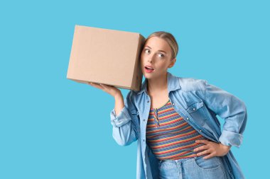 Mavi arka planda paket kutusu olan genç bir kadın.