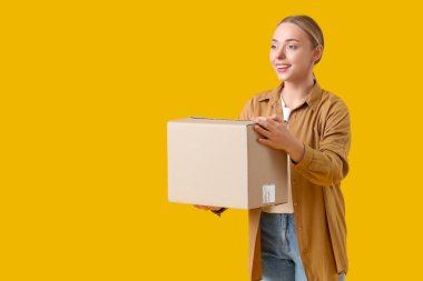 Sarı arka planda paket kutusu olan genç bir kadın.