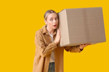 Sarı arka planda paket kutusu olan genç bir kadın.