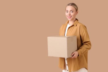 Bej arka planda paket kutusu taşıyan genç bir kadın.