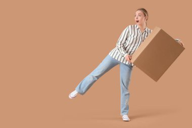 Bej arka planda bir paket kutusu olan şaşırmış genç bir kadın.