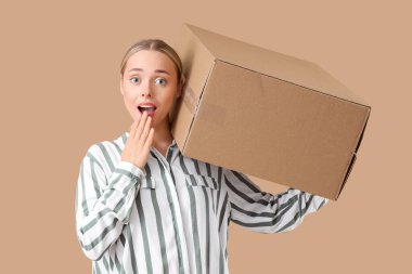 Bej arka planda bir paket kutusu olan şaşırmış genç bir kadın.