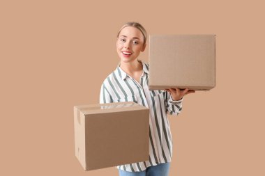 Bej arka planda paket kutuları olan genç bir kadın.
