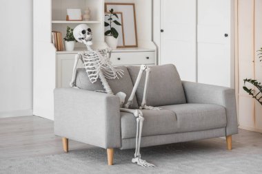 Oturma odasındaki gri koltukta oturan insan iskelet modeli.