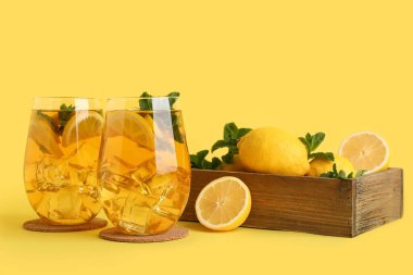 Sarı arka planda nane ve turunçgil meyveli limonlu buzlu çay.