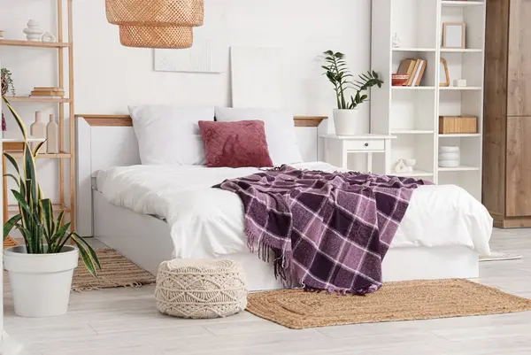 Yatağında raf üniteleri, ev bitkileri ve mor battaniye olan modern yatak odası.